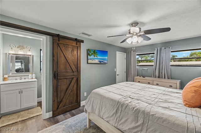 bedroom featuring a barn door, wood finished floors, a sink, baseboards, and ensuite bath