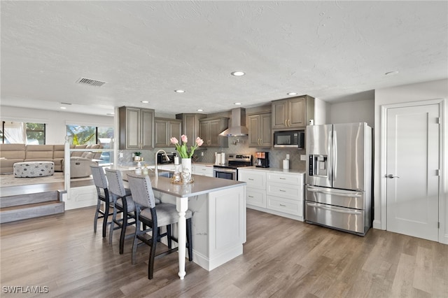 5811 SW 1st Pl, Cape Coral, FL 33914 - kitchen featuring stainless steel appliances, wall chimney exhaust hood, wood finished floors, a kitchen breakfast bar, and a textured ceiling