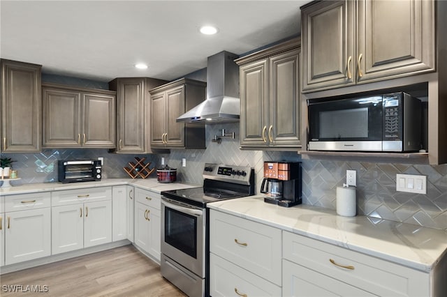 kitchen with stainless steel range with electric cooktop, wall chimney exhaust hood, decorative backsplash, light stone counters, and light wood-type flooring