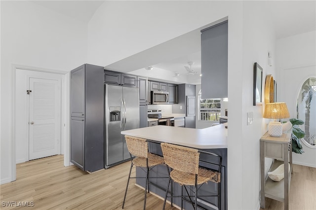 kitchen with gray cabinetry, a kitchen breakfast bar, kitchen peninsula, stainless steel appliances, and light hardwood / wood-style floors