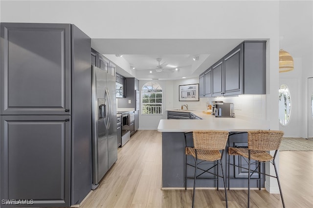 kitchen featuring sink, ceiling fan, a tray ceiling, a kitchen bar, and kitchen peninsula