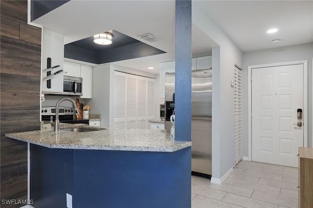 kitchen featuring kitchen peninsula, appliances with stainless steel finishes, light tile patterned flooring, light stone counters, and white cabinetry