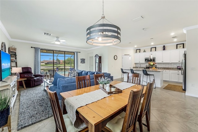 dining area with light tile patterned floors, ceiling fan with notable chandelier, and ornamental molding