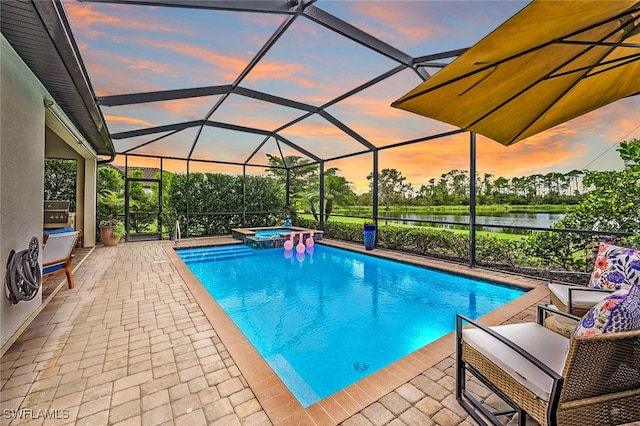 pool at dusk featuring an in ground hot tub, a water view, glass enclosure, and a patio area