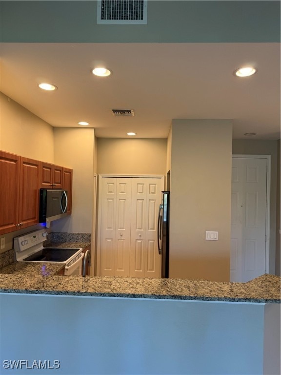 kitchen with kitchen peninsula, electric stove, dark stone counters, refrigerator, and sink