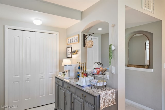 bar featuring gray cabinets, light stone counters, and light tile patterned floors