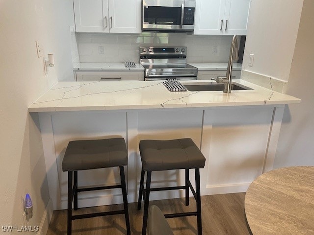 kitchen with light stone counters, dark hardwood / wood-style floors, white cabinetry, a kitchen breakfast bar, and appliances with stainless steel finishes