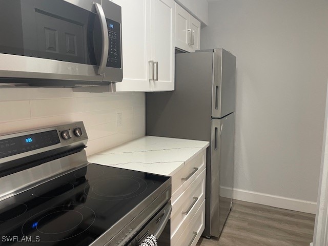 kitchen featuring white cabinets, light stone counters, appliances with stainless steel finishes, and light wood-type flooring