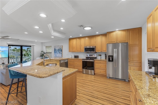 kitchen with sink, a kitchen bar, light hardwood / wood-style flooring, a center island with sink, and appliances with stainless steel finishes