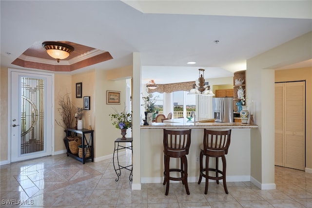 kitchen with kitchen peninsula, stainless steel fridge, a raised ceiling, a breakfast bar area, and crown molding