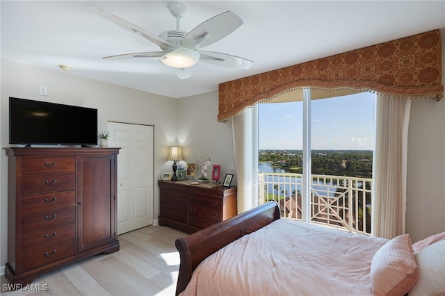 bedroom with a closet, access to outside, light hardwood / wood-style flooring, a water view, and ceiling fan