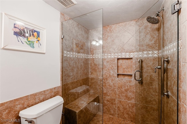 bathroom featuring toilet, a shower with door, and tile walls