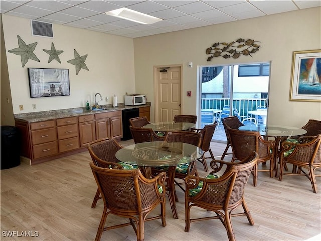 dining space featuring a paneled ceiling, light hardwood / wood-style flooring, and sink