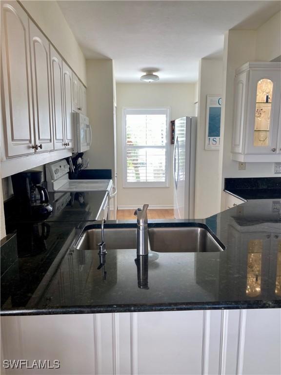 kitchen with sink, kitchen peninsula, dark stone counters, white appliances, and white cabinets