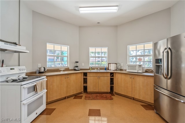 kitchen featuring a towering ceiling, range hood, plenty of natural light, and white appliances