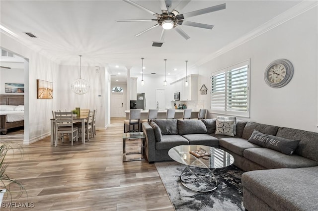 living room with hardwood / wood-style flooring, ornamental molding, and ceiling fan with notable chandelier