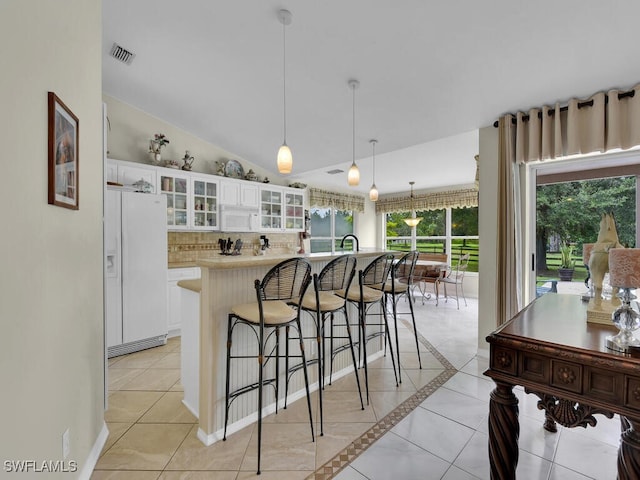 kitchen with vaulted ceiling, light tile patterned floors, white cabinetry, white appliances, and decorative light fixtures