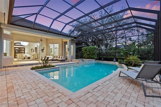 pool at dusk with glass enclosure, ceiling fan, a patio area, and an outdoor hangout area