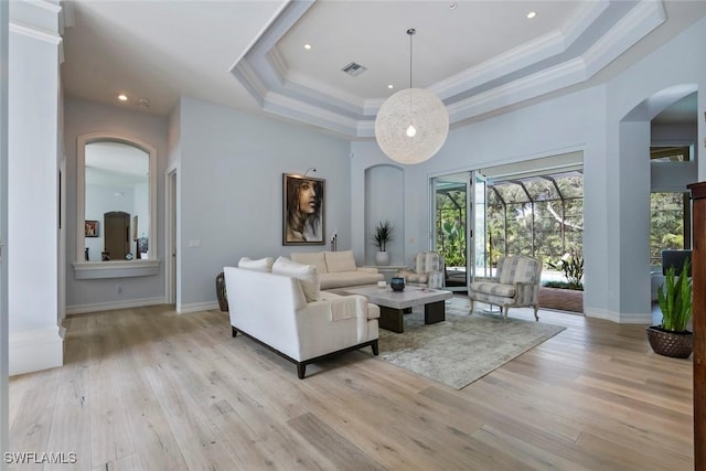 living room featuring a towering ceiling, light hardwood / wood-style flooring, a raised ceiling, and ornamental molding