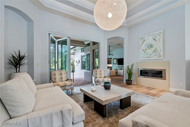 living room with wood-type flooring, crown molding, a towering ceiling, and a tray ceiling