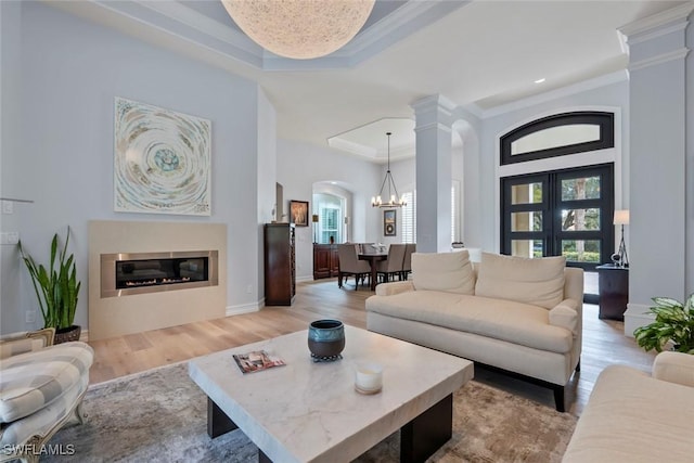 living room featuring a tray ceiling, light hardwood / wood-style floors, a notable chandelier, and ornamental molding