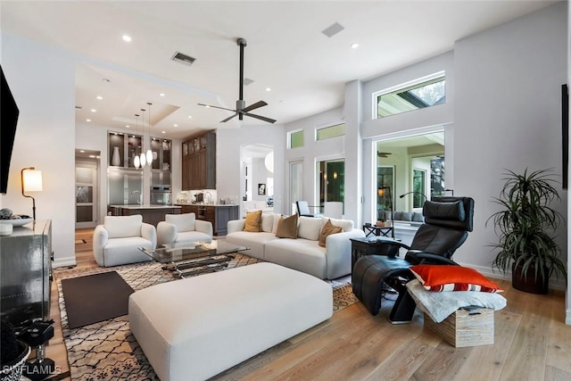 living room featuring a high ceiling, light hardwood / wood-style floors, and ceiling fan