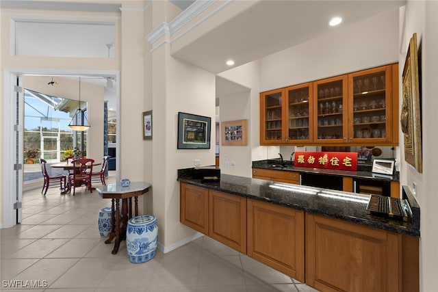 bar with a towering ceiling, dark stone counters, sink, light tile patterned floors, and hanging light fixtures