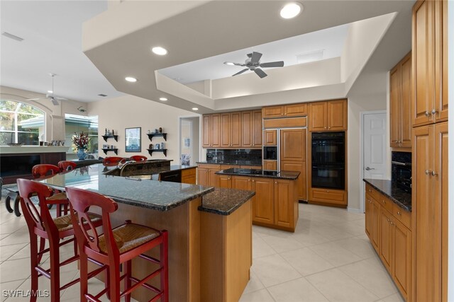 kitchen featuring backsplash, dark stone countertops, kitchen peninsula, a spacious island, and black appliances