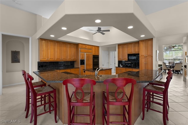 kitchen featuring a kitchen breakfast bar, tasteful backsplash, a tray ceiling, ceiling fan, and light tile patterned floors