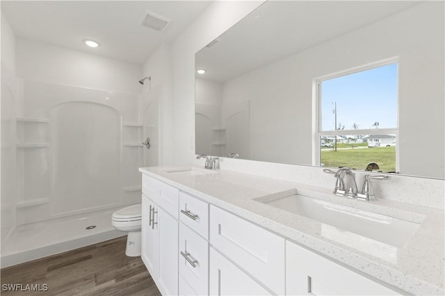 bathroom featuring wood-type flooring, toilet, vanity, and a shower