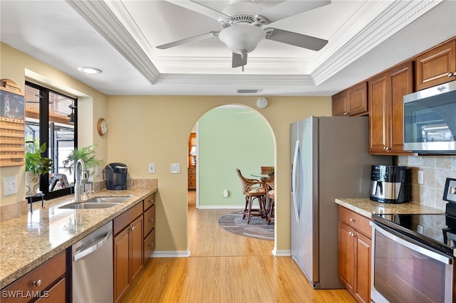 kitchen with stainless steel appliances, sink, light stone counters, and a tray ceiling