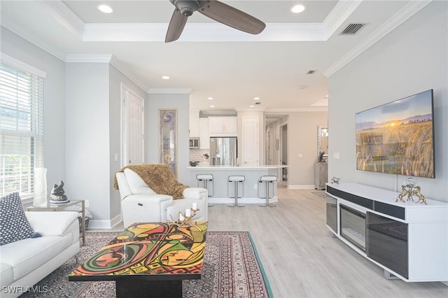 living room featuring light hardwood / wood-style floors, ornamental molding, a tray ceiling, and ceiling fan