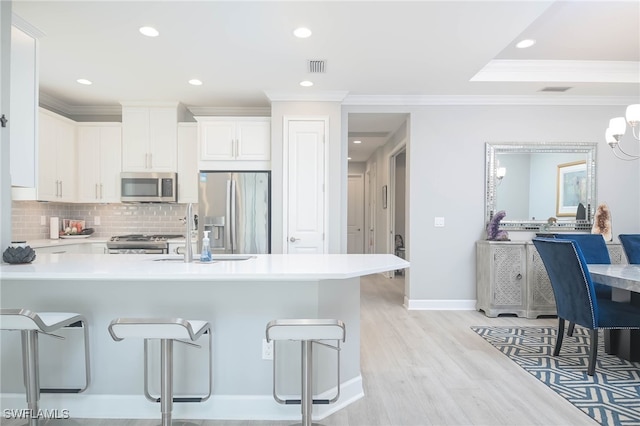 kitchen with a kitchen bar, kitchen peninsula, light hardwood / wood-style floors, stainless steel appliances, and white cabinets