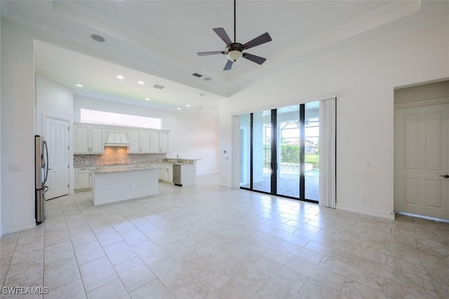 kitchen featuring stainless steel fridge, backsplash, custom range hood, white cabinets, and a kitchen island