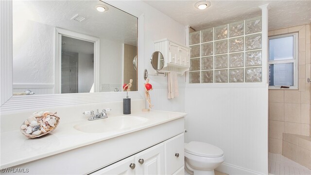 bathroom featuring a tile shower, a textured ceiling, vanity, and toilet