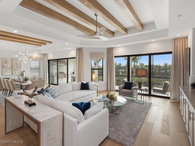 living room with light wood-type flooring, ceiling fan with notable chandelier, and beam ceiling