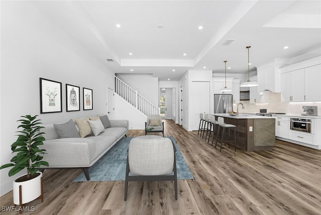 living room featuring light hardwood / wood-style flooring, a tray ceiling, and sink