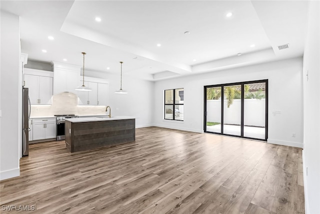 kitchen featuring a kitchen island with sink, white cabinets, light hardwood / wood-style flooring, appliances with stainless steel finishes, and decorative light fixtures