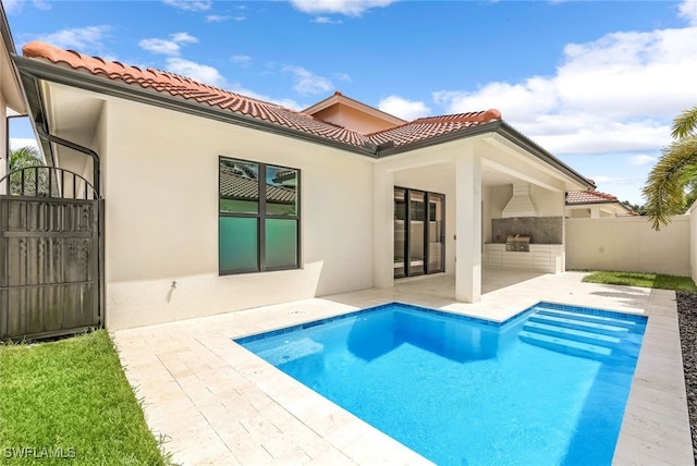 rear view of property featuring a fenced in pool, an outdoor kitchen, and a patio