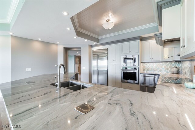 kitchen with light stone countertops, white cabinetry, built in appliances, and sink