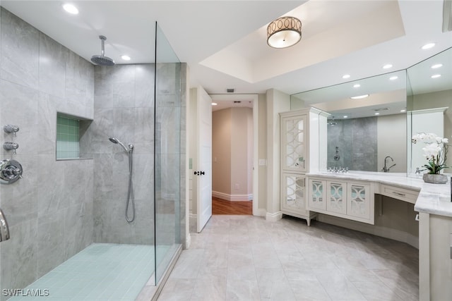 bathroom with a tile shower, vanity, and a tray ceiling