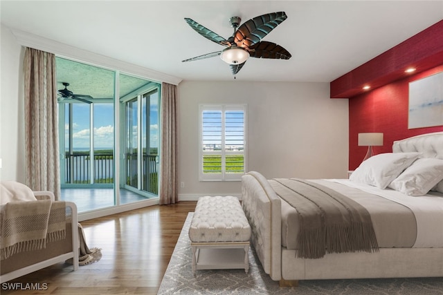 bedroom featuring access to exterior, an accent wall, baseboards, a wall of windows, and wood finished floors