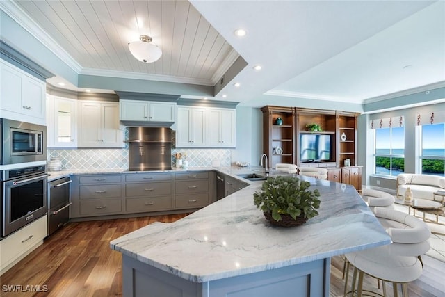 kitchen featuring a peninsula, ornamental molding, gray cabinetry, a sink, and appliances with stainless steel finishes