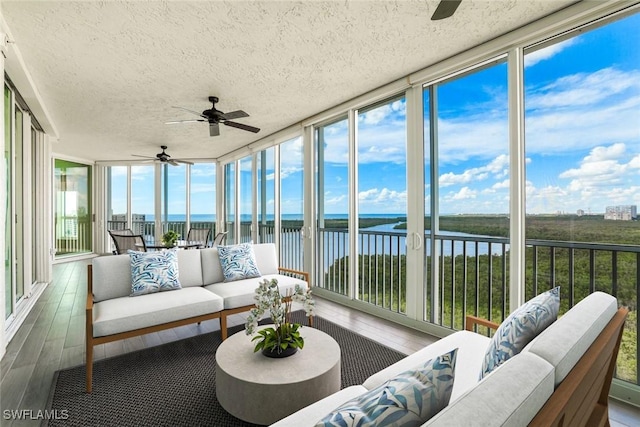 sunroom with ceiling fan and a water view