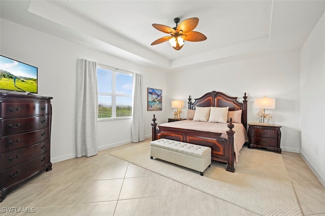 bedroom featuring a ceiling fan, a tray ceiling, baseboards, and light tile patterned floors