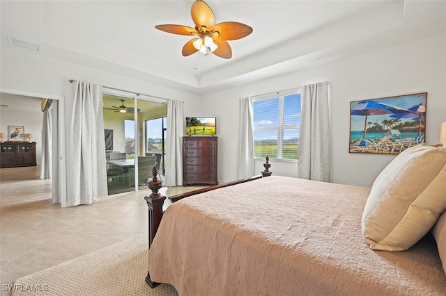 bedroom with light tile patterned floors, multiple windows, a raised ceiling, and access to exterior