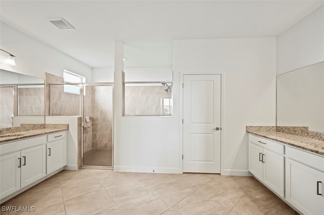 full bathroom featuring a stall shower, visible vents, two vanities, tile patterned flooring, and a sink