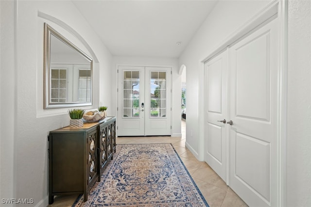 doorway with arched walkways, french doors, light tile patterned floors, and baseboards