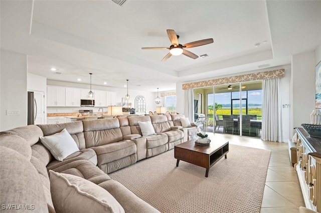 living area with a ceiling fan, a tray ceiling, light tile patterned flooring, and recessed lighting