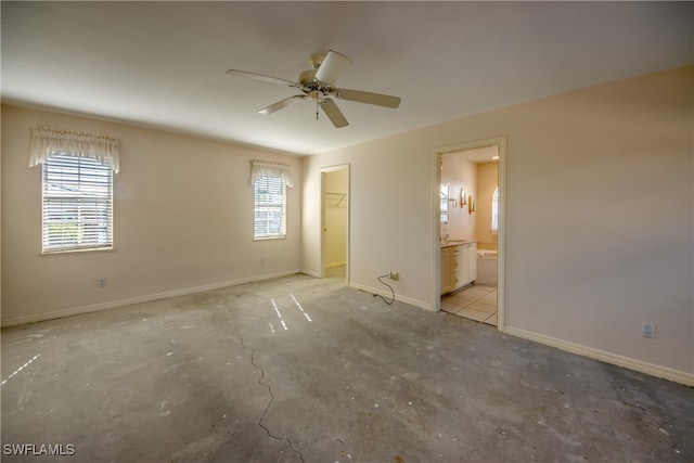 unfurnished bedroom featuring ceiling fan, ensuite bath, multiple windows, and a spacious closet